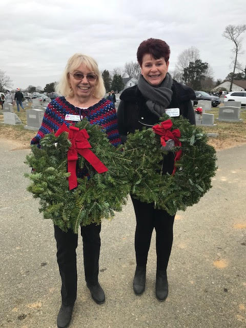 Two women smile and hold Christmas wreaths